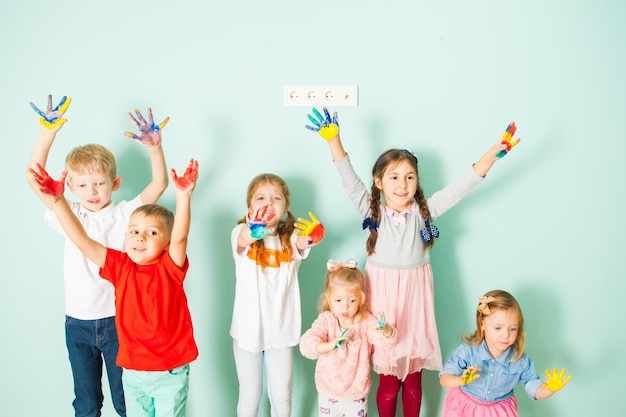 Happy preschoolers and young schoolers standing smiling holding their colored hands up. White background. Creative workshop at waldorf school