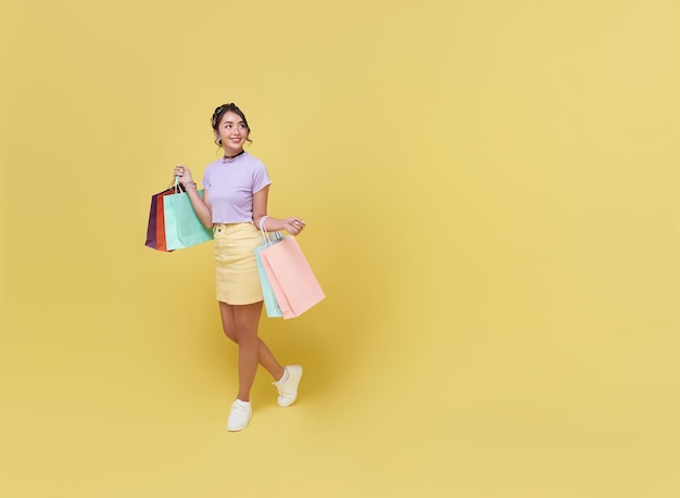 Happy pretty Asian woman carrying colorful shopping bags walking to supermarket