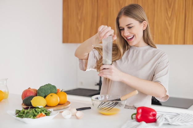 Happy pretty blonde woman in pajamas is preparing breakfast of eggs and salt it among fresh vegetables in the kitchen at home