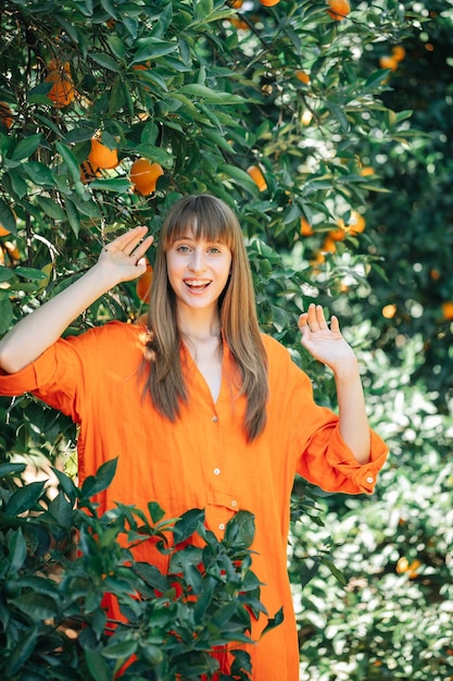 Happy pretty girl in orange dress is looking at camera by holding hands up in orange garden