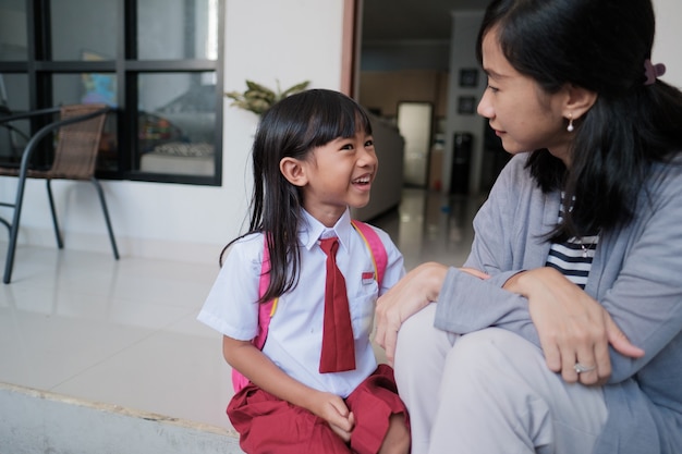 Happy primary student at back home after school and talk to her mother