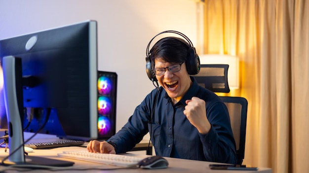 Happy Professional Asian male gamer playing video games on personal pc computer Esport online game