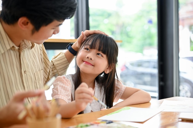 Happy proud Asian dad and daughter having fun together drawing and painting watercolor