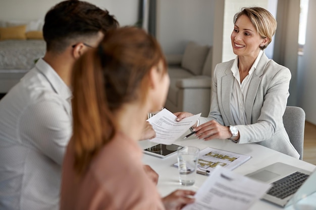 Happy real estate agent having a meeting with a couple and offering them lease agreement to sign