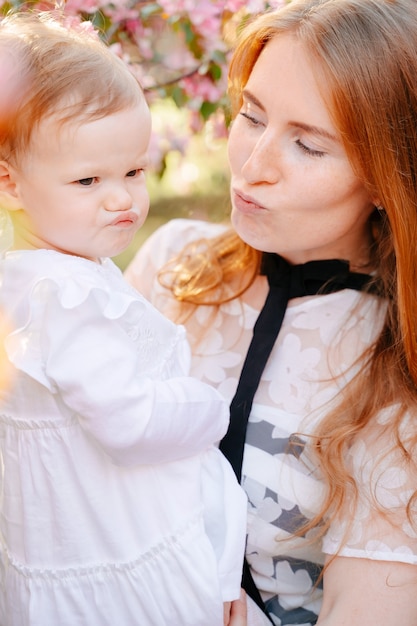 Happy redhaired mother with a baby daughter in her arms fooling around and making faces mothers laziness and march