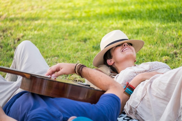 Happy and relaxed cheerful couple laying down on the natural grass and enjoy the outdoor leisure activity with a good weather in spring season man plays a guitar for the lady in romantic concept