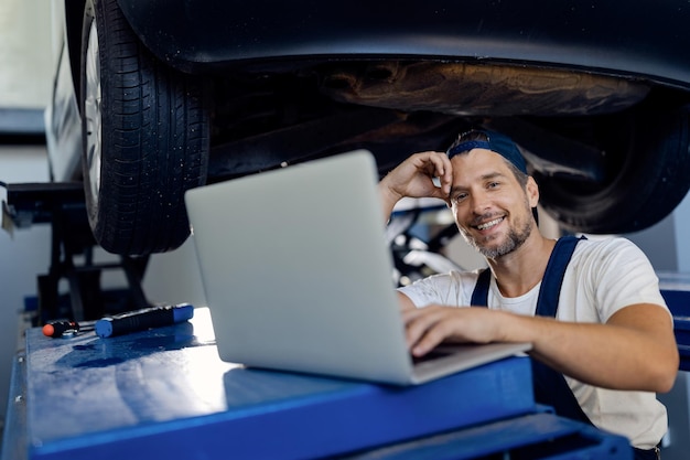 Happy repairman using computer while working at car workshop