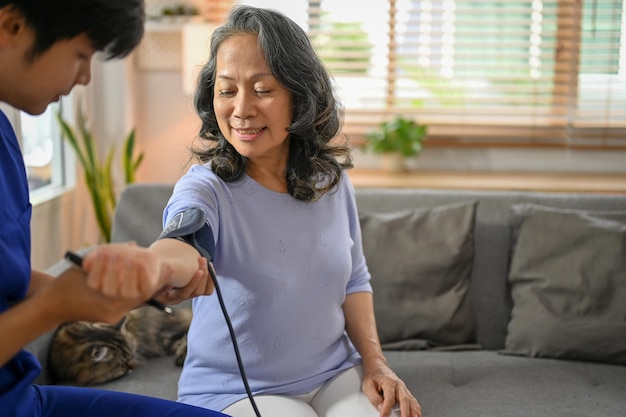 Happy retired Asian woman is being checked for blood pressure with an electric monitor