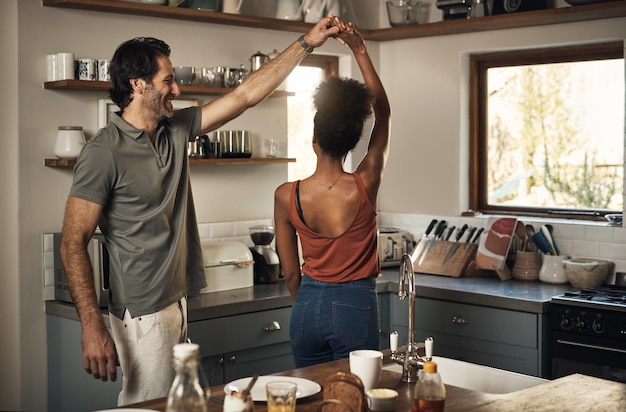 Happy romantic and interracial couple dancing and having fun while bonding in kitchen at home Carefree and energetic loving couple feeling cheerful while sharing a dance and enjoying time together