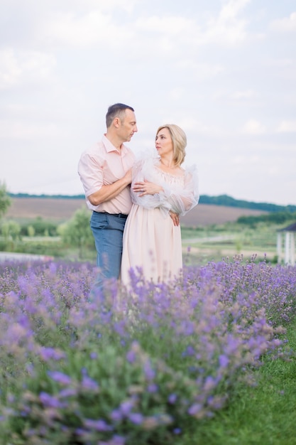 Happy romantic mature couple, posing together looking each other, at beautiful lavender field