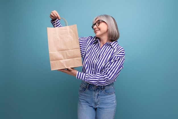 Happy s middle aged woman with gray hair in a stylish look holding a craft bag with a purchase on a