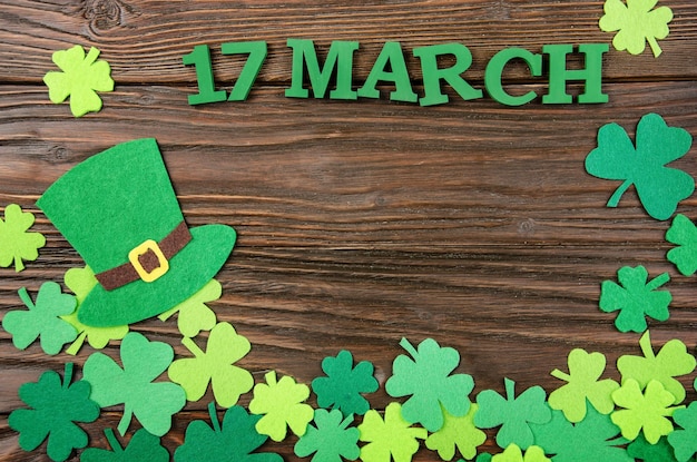 Happy Saint Patrick's mockup of handmade felt hat and shamrock clover leaves on wooden background.