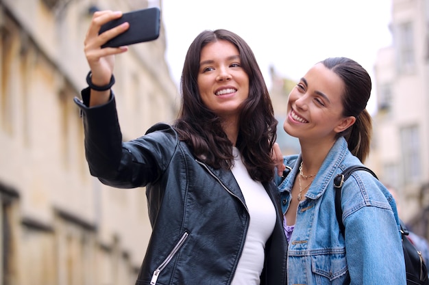 Happy Same Sex Female Couple Sightseeing As They Pose For Selfie And Walk Around Oxford UK Together