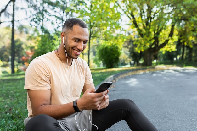 Happy and satisfied man after jogging and fitness class sitting and using smartphone african