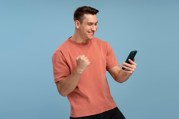 Happy satisfied man in t shirt holding smartphone and smiling making yes gesture