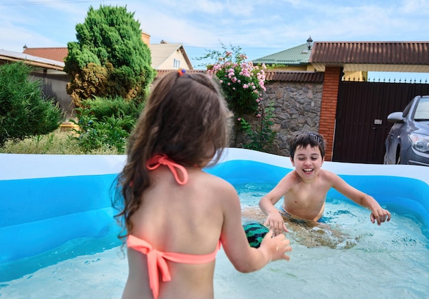 Happy school age kids play ball and splashing each other with water in inflatable swimming pool during summer holidays