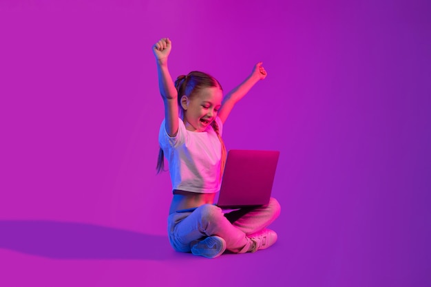 Happy school aged girl playing video games using laptop