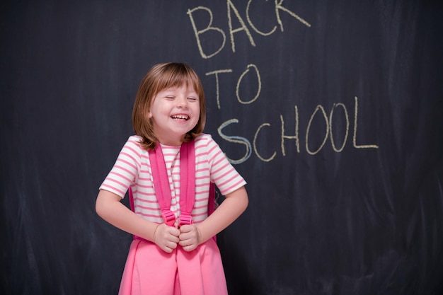 Happy school girl child with backpack writing  back to school on black chalkboard