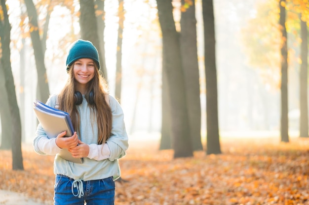 Happy school girl holding folders in autumn park