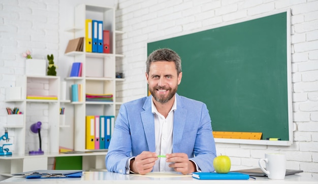 Happy school teacher in classroom at blackboard