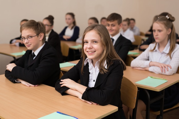 Happy schoolchildren sit at a desk in the classroom