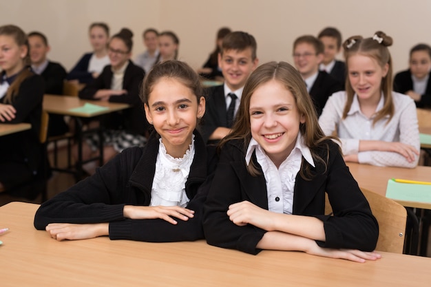 Happy schoolchildren sit at a desk in the classroom