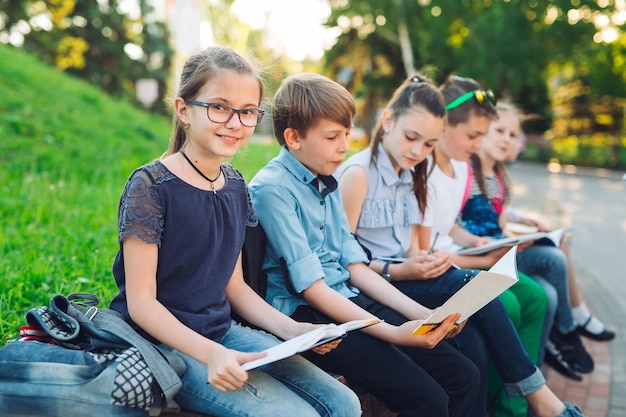 Happy Schoolmates Portrait. Schoolmates seating with books in a wooden bench in a city park and studying on sunny day.