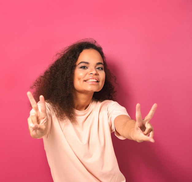 Happy sending peace gesture with two hands beautiful young african american woman looking positively...