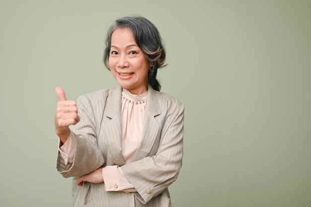 Happy senior Asian woman showing thumb up isolated green background Good job Excellent Great