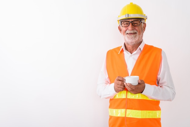 happy senior bearded man construction worker smiling and holding coffee cup while wearing eyeglasses on white