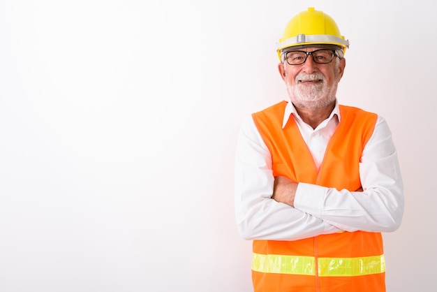 happy senior bearded man construction worker smiling and wearing eyeglasses with arms crossed on white