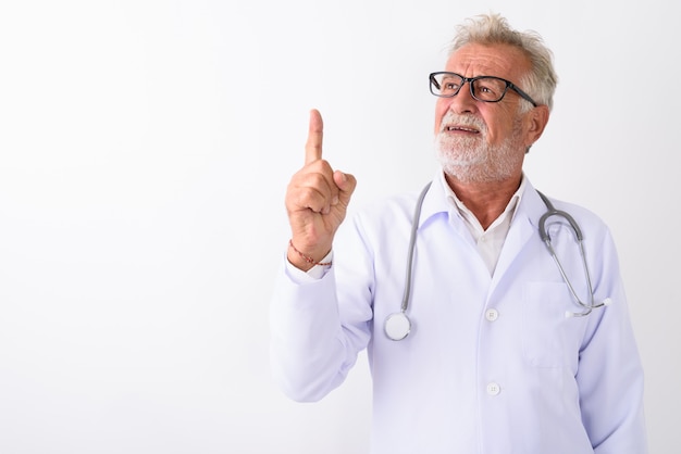 happy senior bearded man doctor smiling and thinking while pointing finger up on white