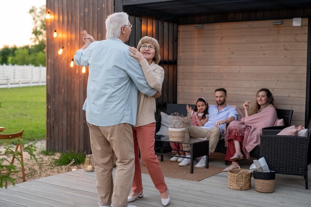 Happy senior couple dancing on patio in front of their family