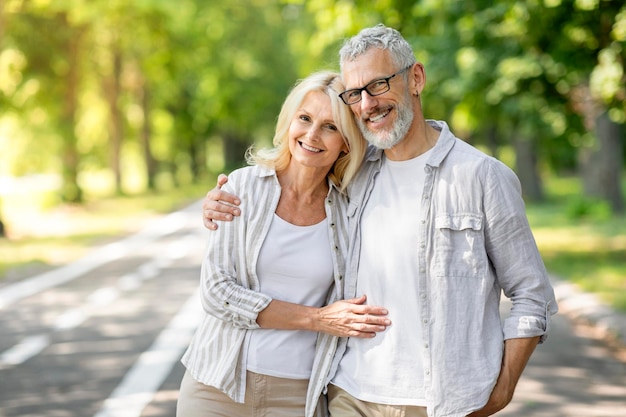 Happy senior couple embracing and smiling to camera while posing together outdoors