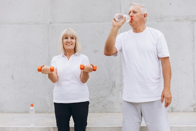 Photo happy senior couple exercising outdoors with dumbbells and drinking water