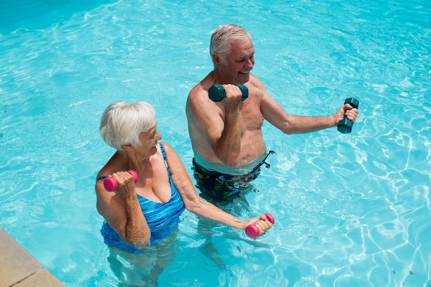 Happy senior couple exercising with dumbbells in the pool