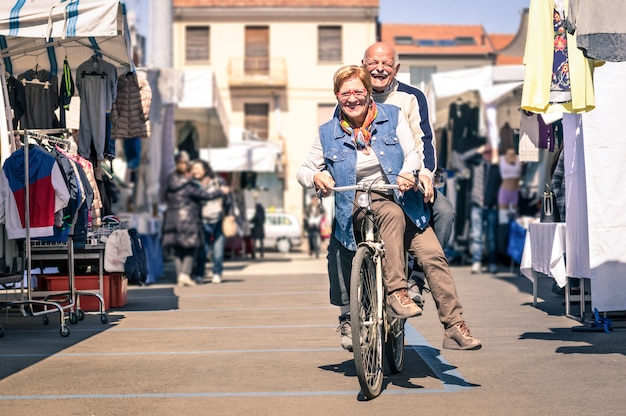 Happy senior couple having fun with bicycle at flea market