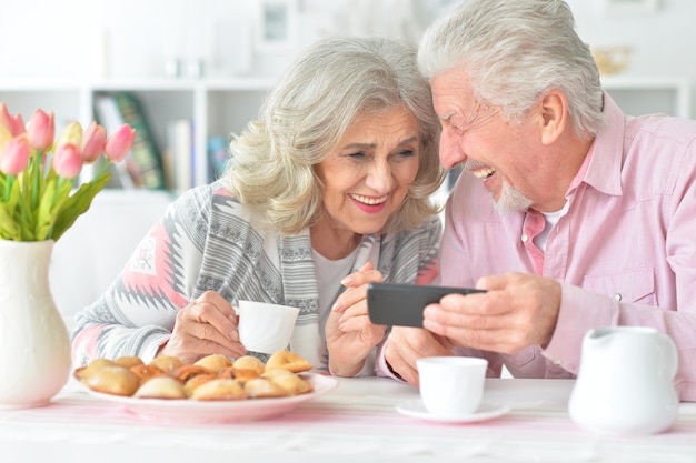 Happy senior couple looking at smartphone while drinking tea at kitchen