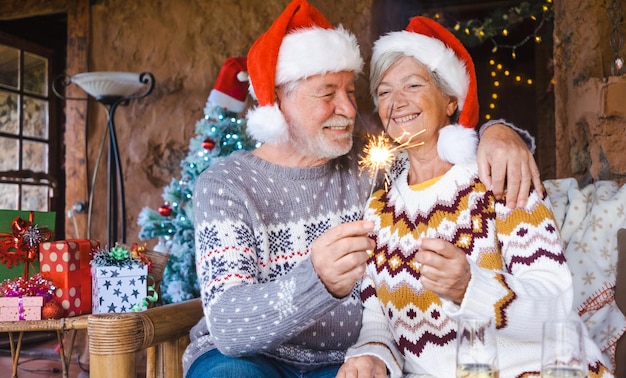 Happy senior couple in Santa hats smiling and hugging at home at Christmas time with sparklers Christmas Family Love concept