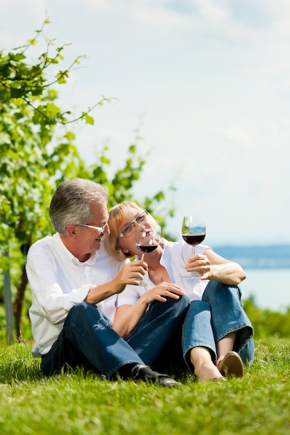 Happy senior couple sitting in the grass drinking wine 