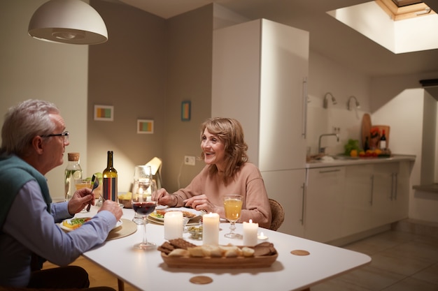 Happy senior couple sitting at the table in domestic kitchen they have festive dinner