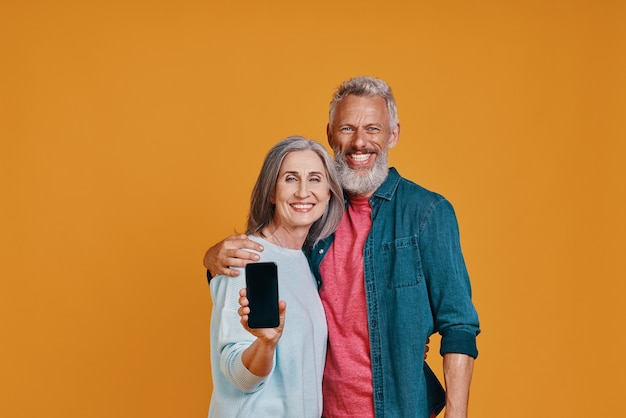 Happy senior couple smiling and showing smart phone 