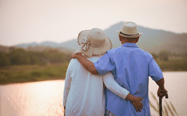 A happy senior couple standing near mountain and lake during sunset