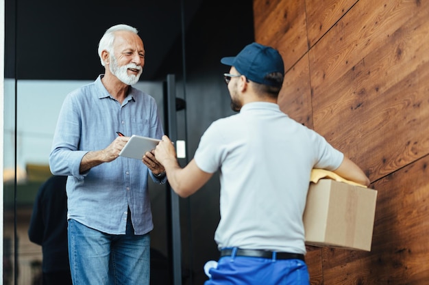 Happy senior man communicating with a courier while signing for delivery on touchpad