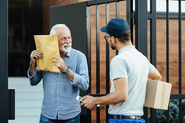 Happy senior man getting a delivery from courier and feeling curious what is inside of a package