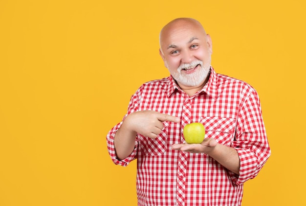 Happy senior man or grandfather in checkered shirt with apple on yellow background