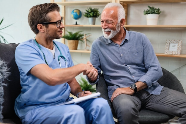 Happy senior man shaking hands with a doctor who is being in a home visit