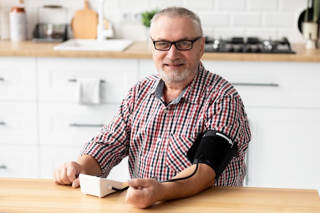 Happy senior man using medical device to measure blood pressure