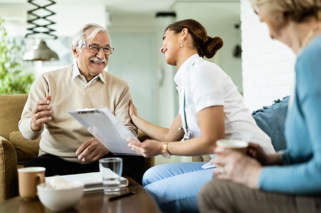 Happy senior man and young female doctor talking during home visit