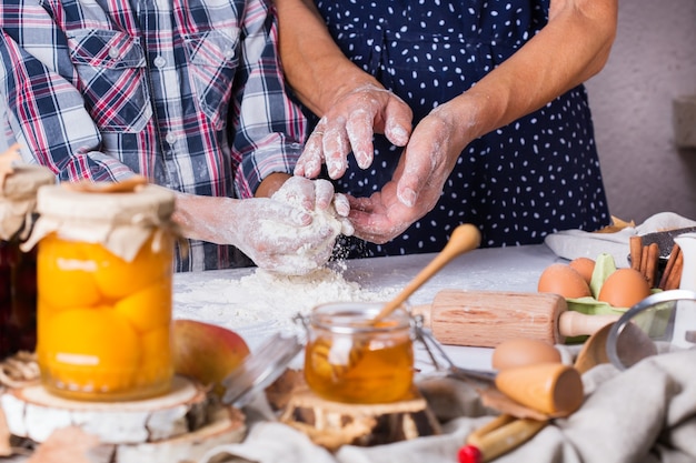 Happy senior mature woman, grandmother and young boy, grandson cooking, kneading dough, baking pie, cake,  cookies. Family time in the cozy kitchen. Autumn activity at home.